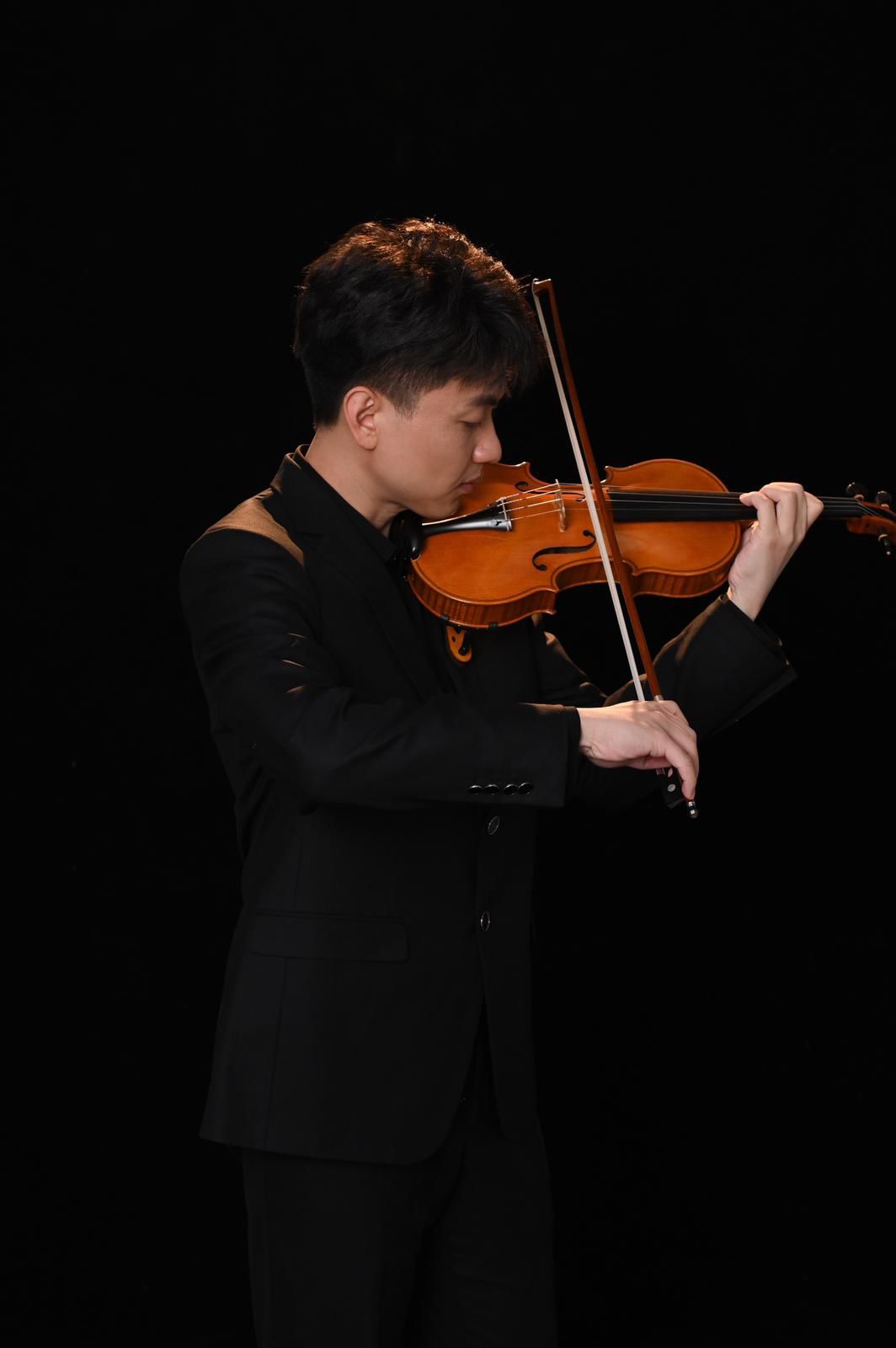 Han Xingzhi in a black suit playing the violin against a black background, with his hands, bow and violin shown as photographed.